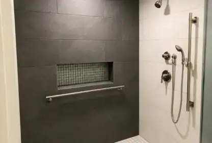 Modern walk-in shower with dark and light tiles, built-in niche with small tiles, grab bar, rainfall showerhead, and handheld showerhead with controls.