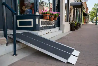 A portable wheelchair ramp provides access to a storefront entrance with a single step on a brick-paved sidewalk.