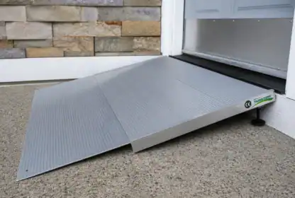 A portable metal wheelchair ramp is placed at a doorstep, providing accessible entry into a building with a small step.