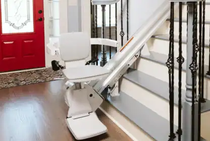 A motorized stair lift installed on a residential staircase with a red front door and wooden floor visible in the entryway.