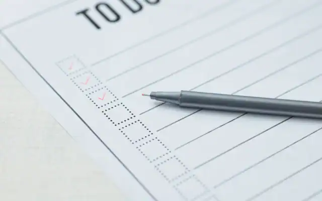 A pen rests on a blank to-do list, with a few checkboxes at the top marked with red check marks.