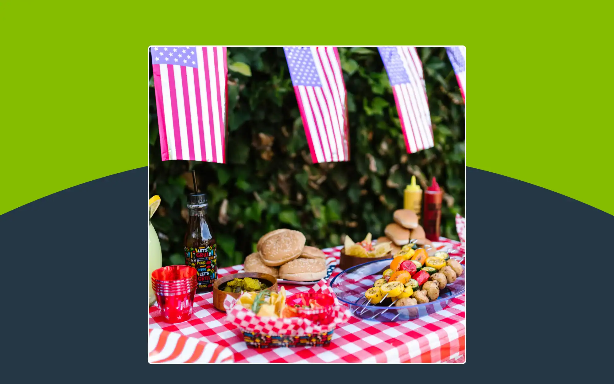 A picnic table with burgers, skewers, condiments, and drinks on a red checkered tablecloth, decorated with hanging American flags.