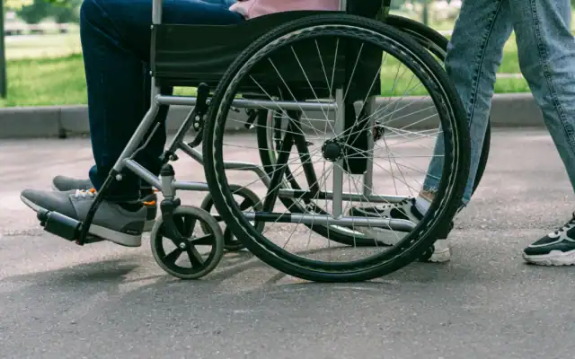 A person in a wheelchair is being pushed by another individual outdoors on a paved path.