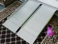 A portable metal wheelchair ramp is placed over a threshold on top of a patterned carpet, leading into a doorway.
