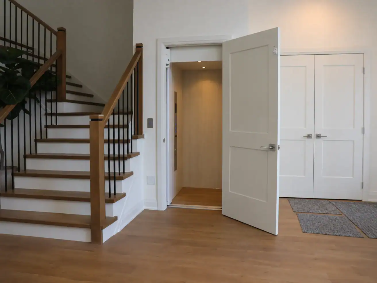 A modern home interior features a wooden staircase, an open residential elevator, double doors, and hardwood flooring.