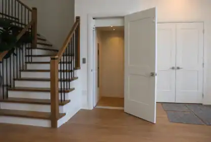 A modern home interior features a wooden staircase, an open residential elevator, double doors, and hardwood flooring.