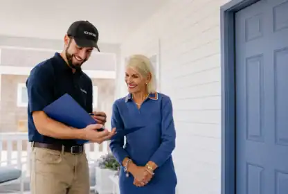 A man in a uniform shows documents to a woman standing next to him on a porch near a blue door.