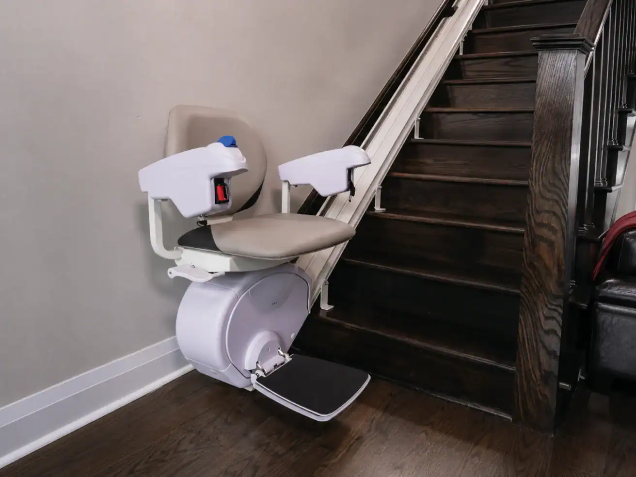 A stairlift with a padded seat and armrests is installed beside a dark wooden staircase in a residential setting.
