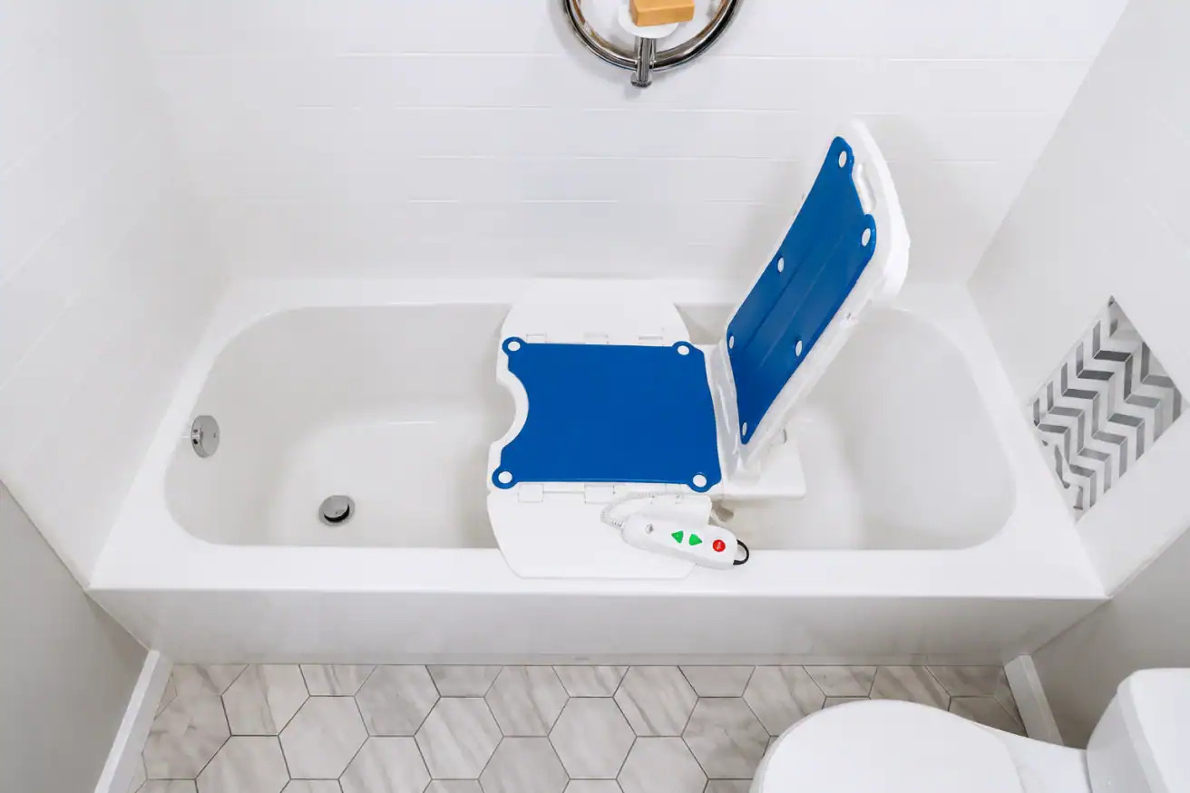 A bathtub with a blue and white electric bath lift chair inside, surrounded by white tile walls and hexagonal floor tiles.
