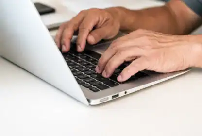 Close-up of a person's hands typing on a laptop keyboard on a white desk.