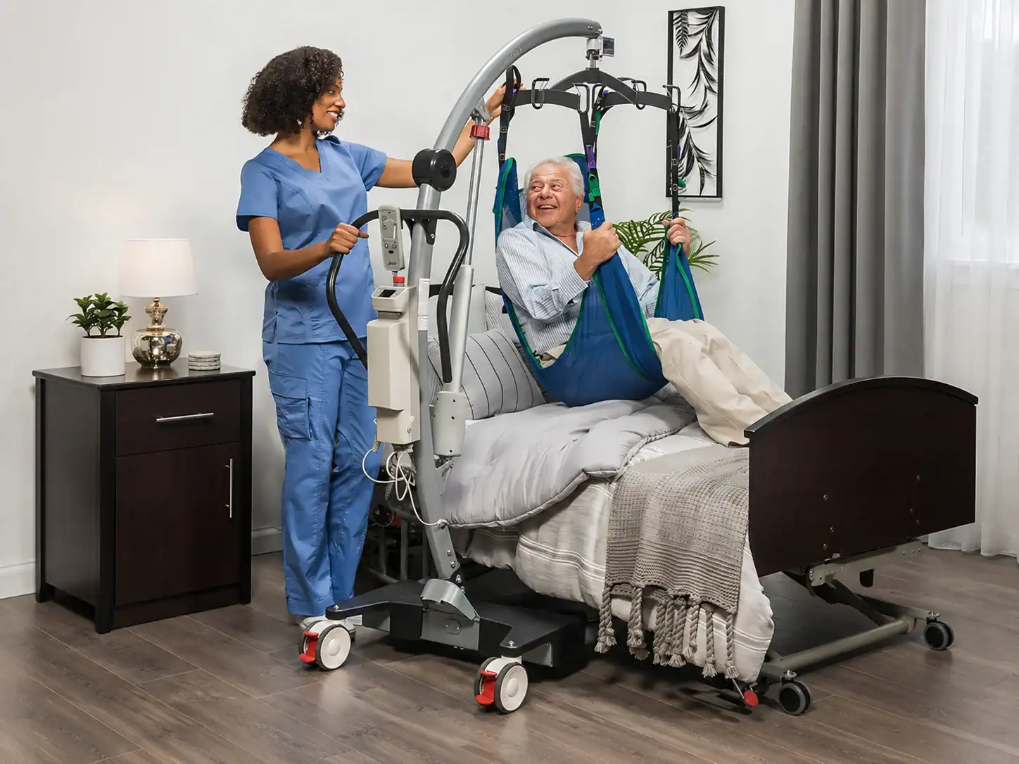 A nurse uses a patient lift to transfer an elderly man from a hospital bed in a well-lit, modern room.