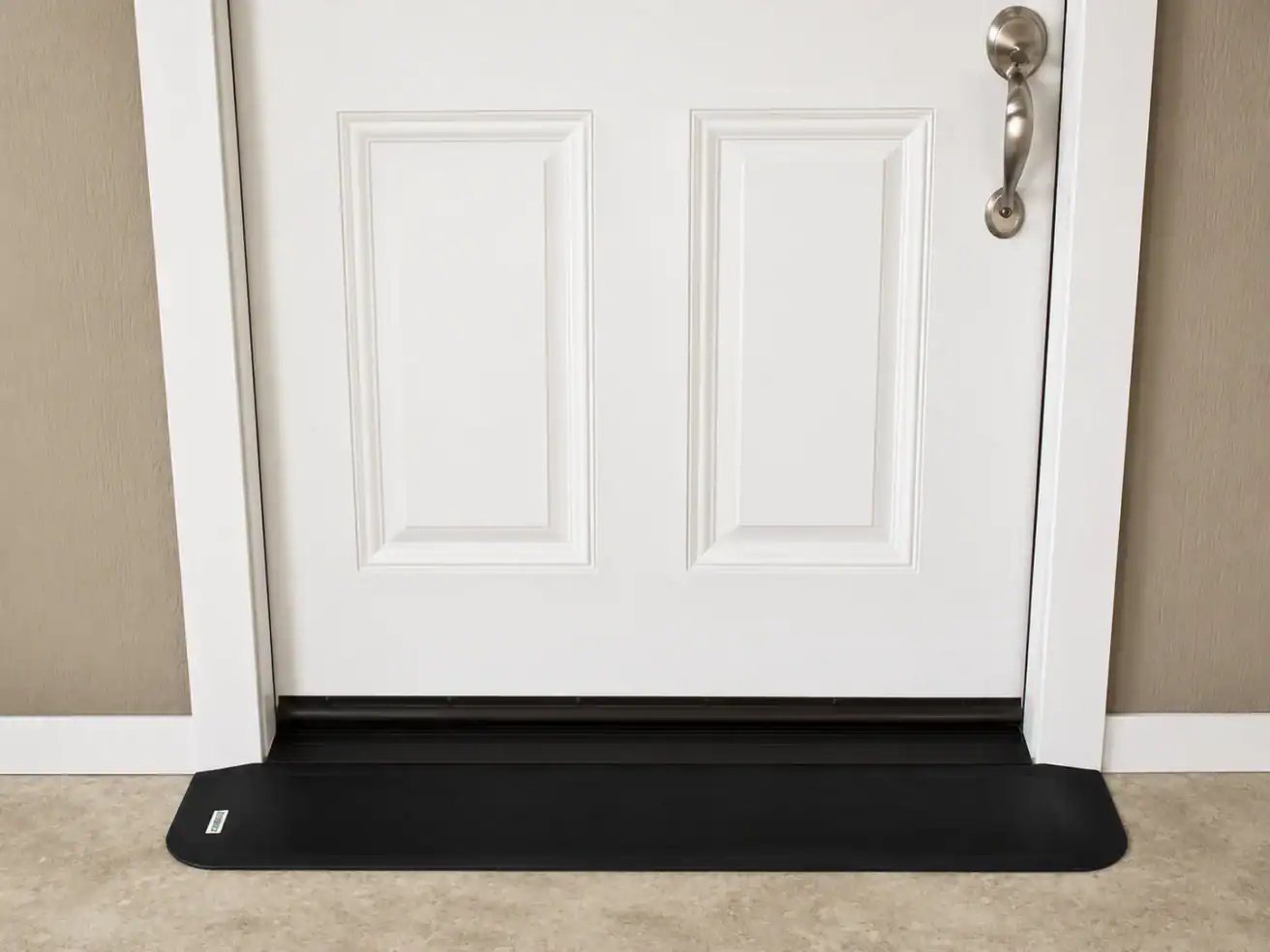 A white door with a silver handle is closed, with a black draft stopper placed along the bottom edge on a light-colored floor.
