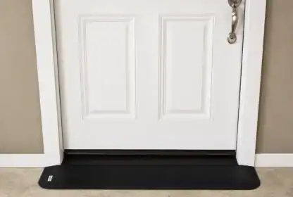 A white door with a silver handle is closed, with a black draft stopper placed along the bottom edge on a light-colored floor.