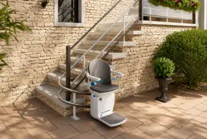 A stairlift is installed along an outdoor staircase with a stone wall and metal railing, providing accessibility between the patio and the elevated entrance.
