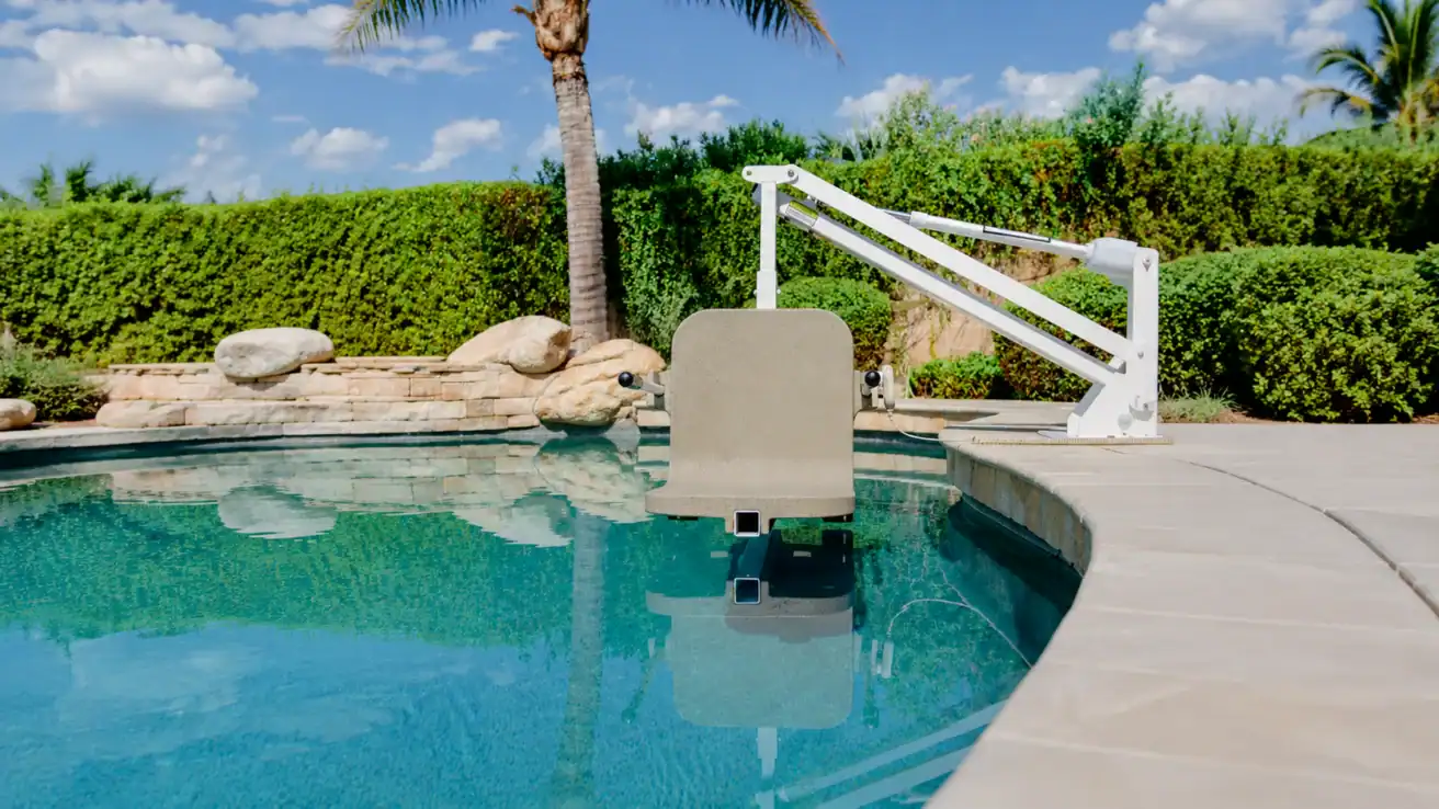 A poolside mechanical lift chair is positioned over the water, designed to assist individuals with mobility needs in entering and exiting the swimming pool.