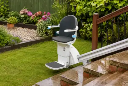 Outdoor stairlift installed on a garden staircase, next to a wet lawn and flower beds, on a rainy day.
