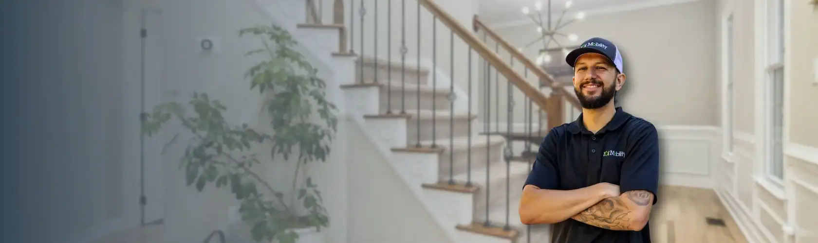 Man in a black polo and cap stands smiling with arms crossed in front of a staircase inside a well-lit, modern home.
