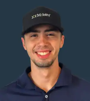Young man with short facial hair, wearing a black "101 Mobility" cap and a navy blue collared shirt, smiling against a plain dark background.