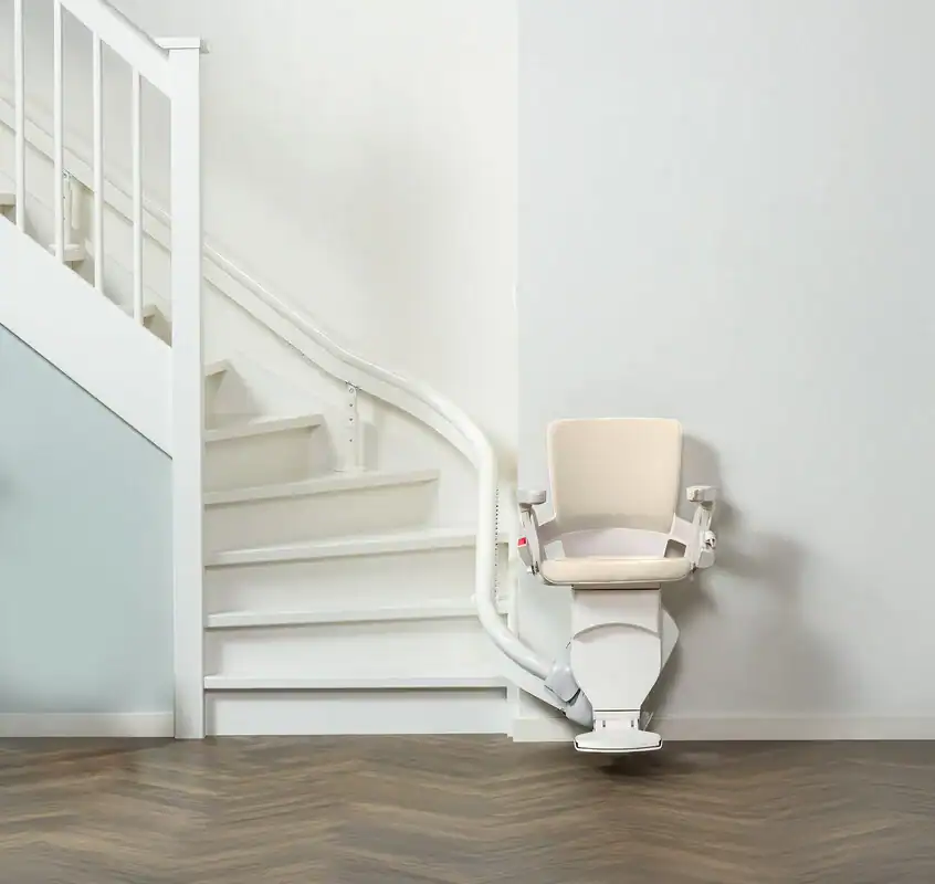 A stairlift attached to a white staircase, featuring a padded seat and armrests, installed along the curved wall for accessibility.