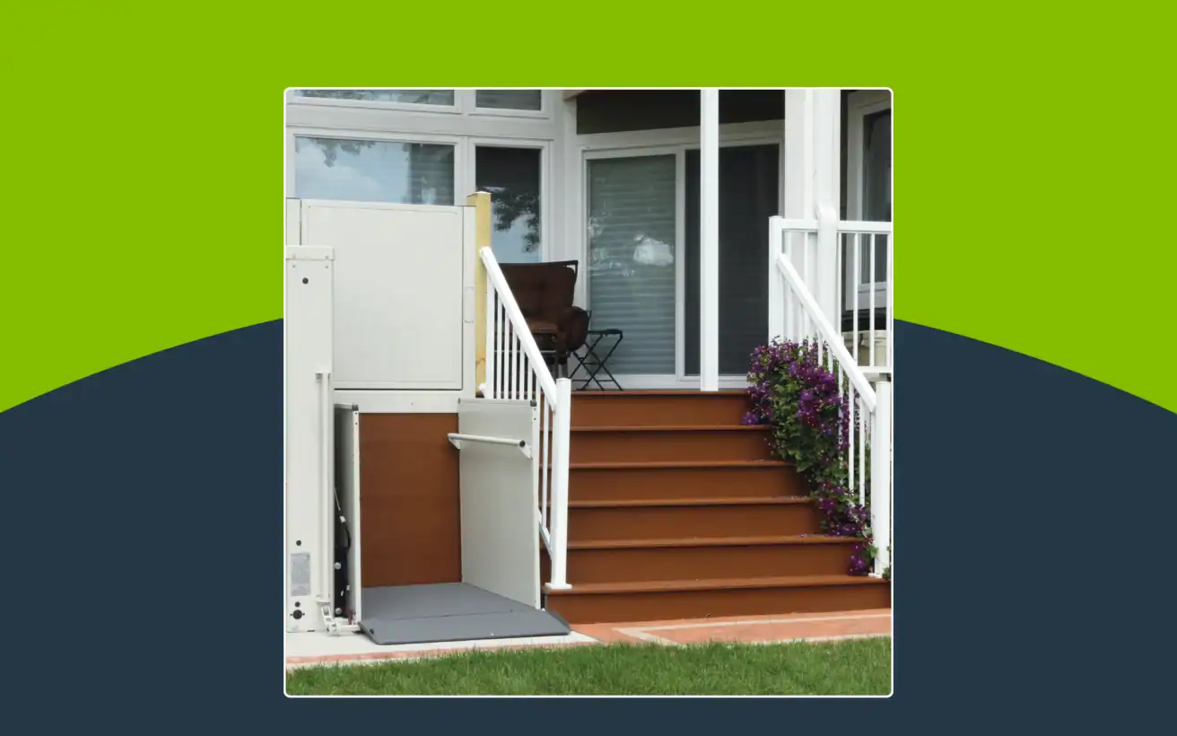 A porch lift is installed next to a set of stairs leading to a home's front door, with railings and potted flowers on the steps.