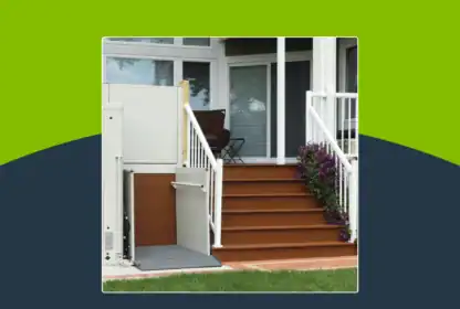 A porch lift is installed next to a set of stairs leading to a home's front door, with railings and potted flowers on the steps.