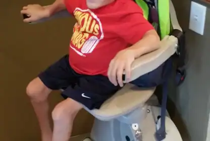 A smiling young boy sits on a stairlift with a green backpack. A quote about support for families appears at the bottom of the image.