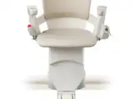 Front view of a beige and white motorized stair lift chair with armrests, mounted on a straight rail track, isolated on a white background.