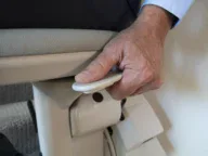 A person grips a curved lever on the side of a light-colored chair, possibly adjusting the seat position or height.