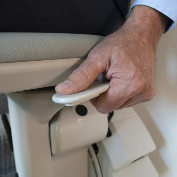 A person grips a curved lever on the side of a light-colored chair, possibly adjusting the seat position or height.