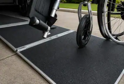 A wheelchair is being rolled down a portable ramp onto a concrete sidewalk.