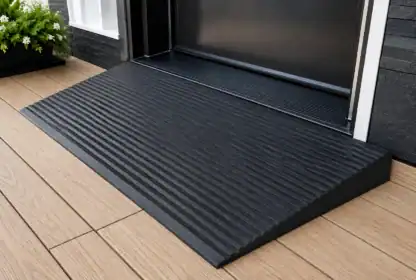 A black rubber threshold ramp with ridges leads from a wooden deck into a doorway, providing accessible entry.