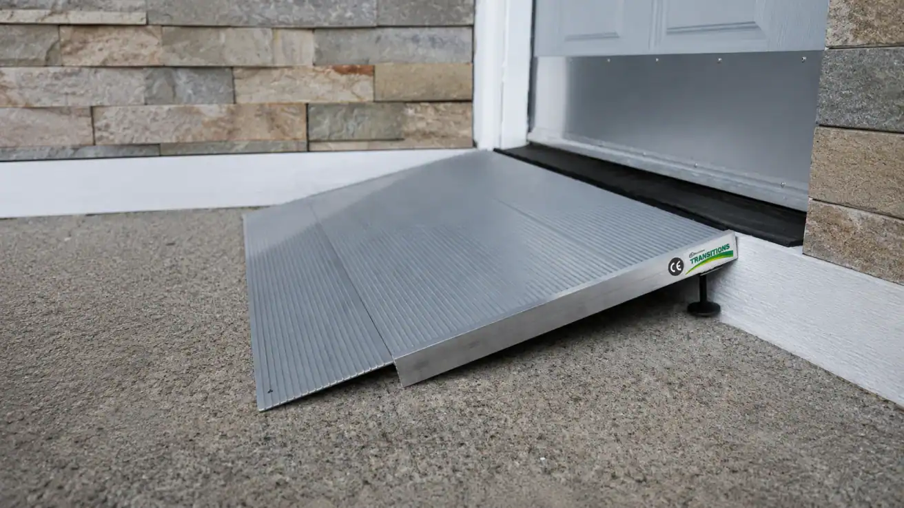 A portable metal wheelchair ramp is positioned at the base of a step leading to a closed door, providing accessible entry to the building.