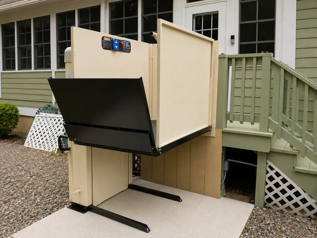 A beige wheelchair lift is installed next to green steps, providing access from the ground level to a porch door of a house.