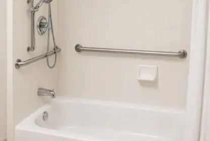 White bathtub with a showerhead, faucet, two metal grab bars, a soap dish, and white tiled walls.
