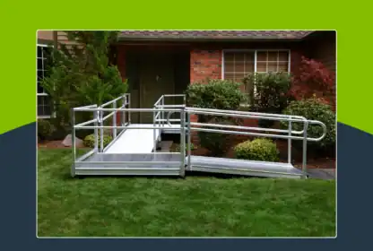 A metal wheelchair ramp is installed over a grassy yard, leading to the front door of a brick house with shrubs and trees nearby.
