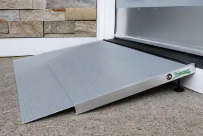 A metal wheelchair ramp is positioned at the entrance of a building, providing access over a doorstep onto a concrete surface.