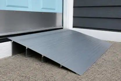 A metal wheelchair ramp is placed at the entrance of a light blue door, providing access over a step on a concrete surface.
