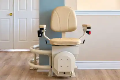 A beige stairlift mounted on a curved rail at the bottom of a staircase.