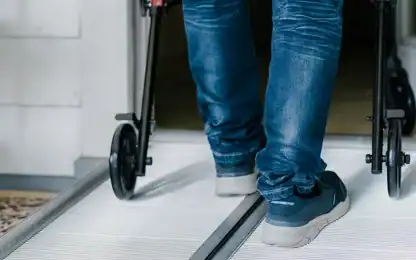 A person wearing jeans uses a walker to move up a wheelchair-accessible ramp indoors.