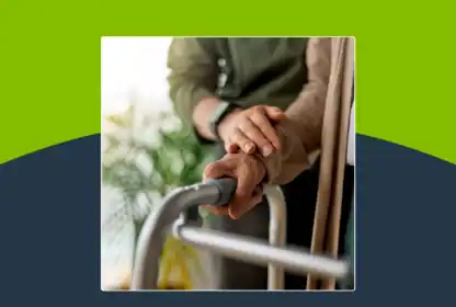 Two people’s hands rest on a walker, with one person offering support to the other. The background is blurred with greenery visible.