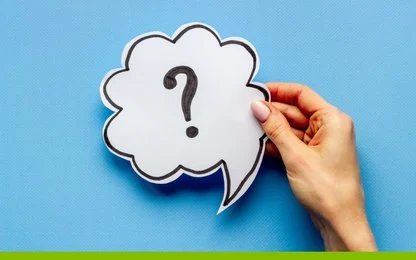 A hand holds a paper cutout of a speech bubble with a large question mark on it, against a blue background with a green stripe at the bottom.