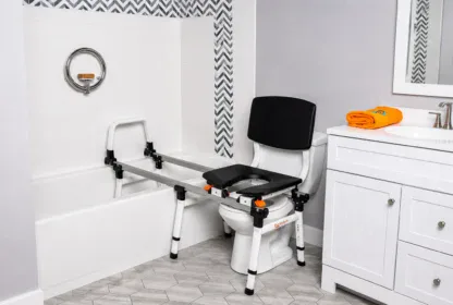 Transfer bench with a sliding seat positioned over a bathtub and toilet in a modern bathroom with gray and white decor.