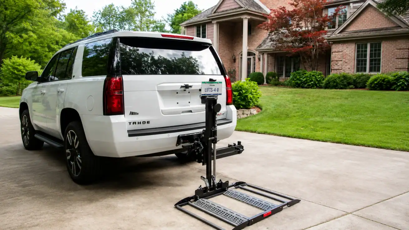 A white Chevrolet Tahoe with a hitch-mounted mobility scooter lift is parked in a driveway in front of a brick house with green landscaping.