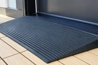 A black, ribbed wheelchair ramp leads up to a door from a light wood deck, providing accessible entry to the building.