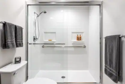 Modern bathroom with a glass-enclosed shower, white tile walls, two built-in shelves, chrome fixtures, and three dark gray towels on racks.