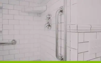 White tiled shower with chrome grab bars, two control knobs, a corner shelf, and a light switch on the right wall.