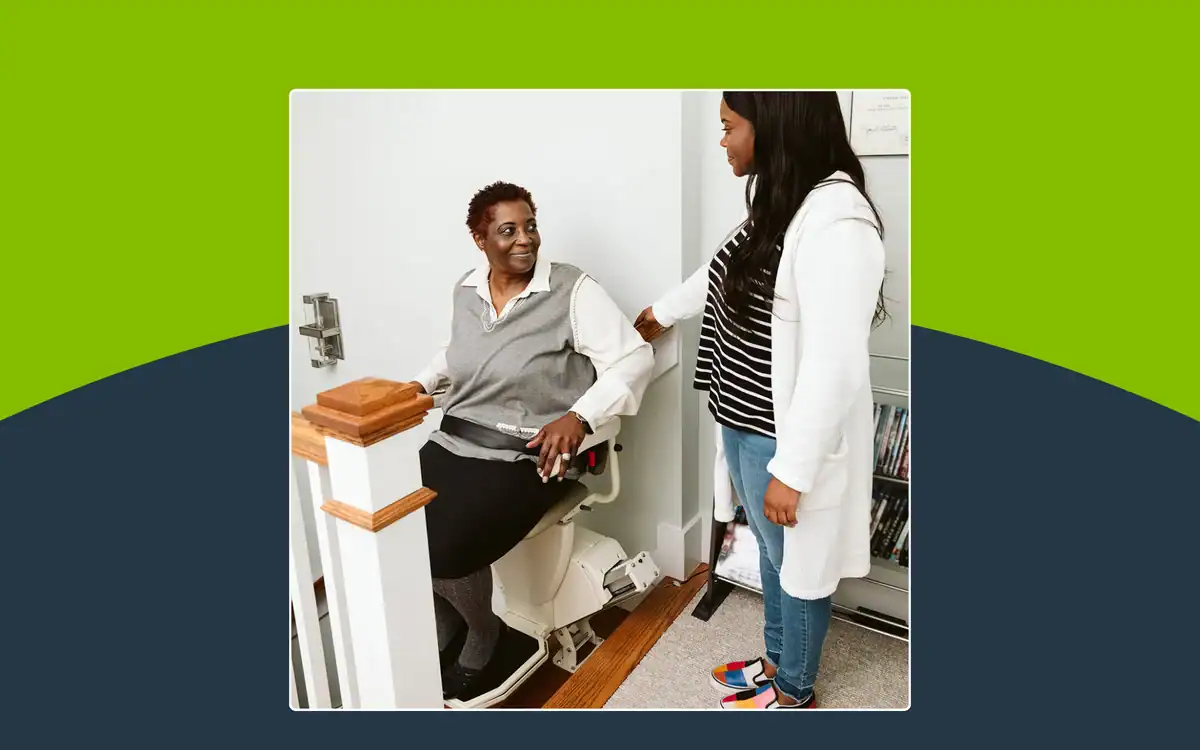 A caregiver standing next to an older woman seated on a stairlift.