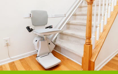 A motorized stair lift installed on a carpeted staircase with a wooden handrail.
