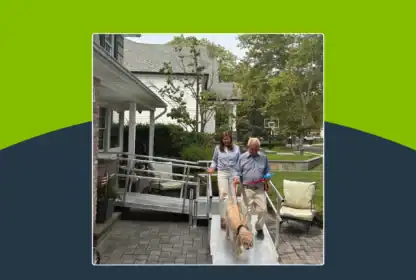 An older man and a woman walk a golden dog down an ADA-compliant metal wheelchair ramp at a residential home.