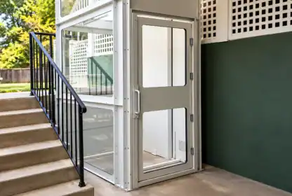 A white residential platform lift installed outdoors next to a concrete staircase.
